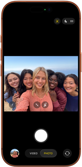 iPhone 17 Pro en naranja cósmico, frente, la pantalla muestra la cámara frontal Center Stage abierta con una selfie grupal de cinco personas centradas en el encuadre 