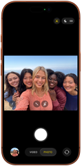 iPhone 17 Pro en naranja cósmico, frente, la pantalla muestra la cámara frontal Center Stage abierta con una selfie grupal de cinco personas centradas en el encuadre 