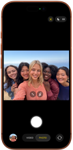 iPhone 17 Pro en naranja cósmico, frente, la pantalla muestra la cámara frontal Center Stage abierta con una selfie grupal de cinco personas centradas en el encuadre 