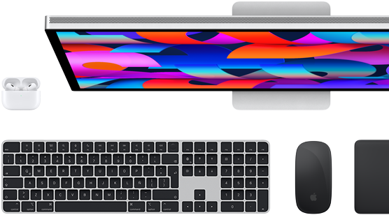 Vista desde arriba de un monitor Studio Display, un Magic Keyboard negro, un Magic Mouse negro, un Magic Trackpad negro y un estuche blanco para los AirPods